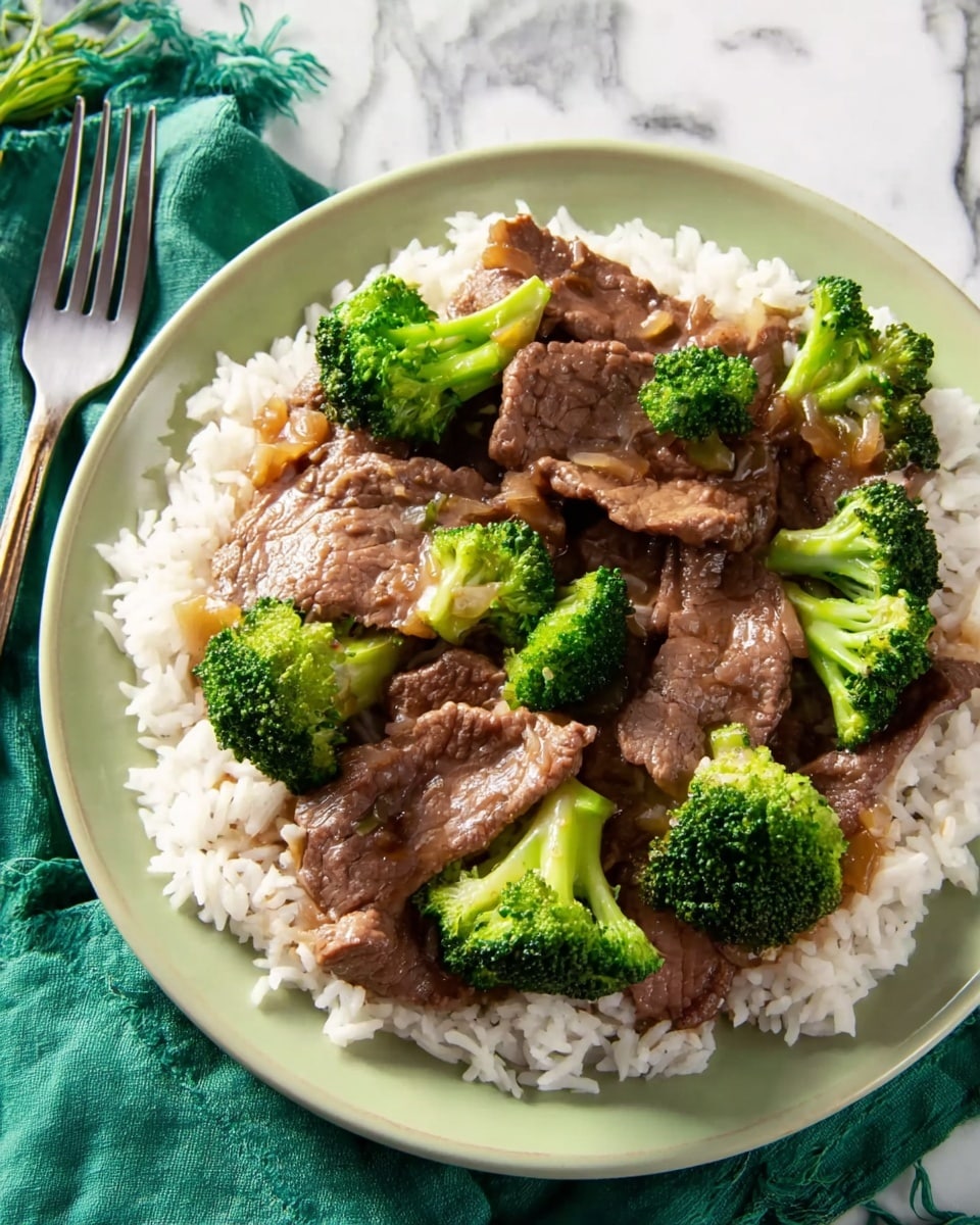 A white plate holds a serving of white rice as the base layer, topped with tender brown slices of beef evenly spread across the rice. Bright green broccoli florets are placed between the beef pieces, adding fresh color and texture. The beef appears slightly glossy with a thin sauce coating. The plate rests on a white marbled surface with a green cloth napkin and a fork placed to the left side. Photo taken with an iphone --ar 4:5 --v 7