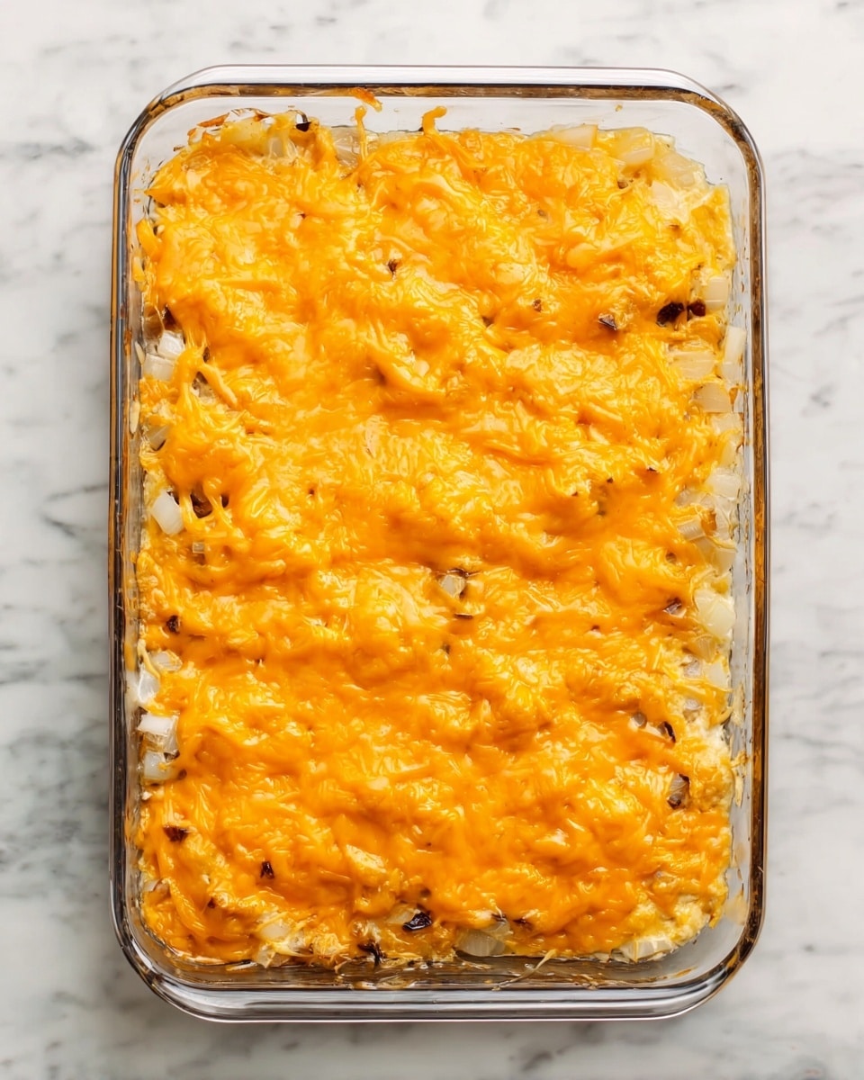 A rectangular glass baking dish sits on a white marbled surface filled with a two-layered casserole. The bottom layer is made of chopped white onions scattered unevenly, and the top layer consists of melted bright orange cheddar cheese that covers the onions completely with a slightly bubbly and browned texture in some areas. The edges of the glass dish are clean, and a few cheese drips hang over the sides. The scene looks warm and homemade. photo taken with an iphone --ar 4:5 --v 7