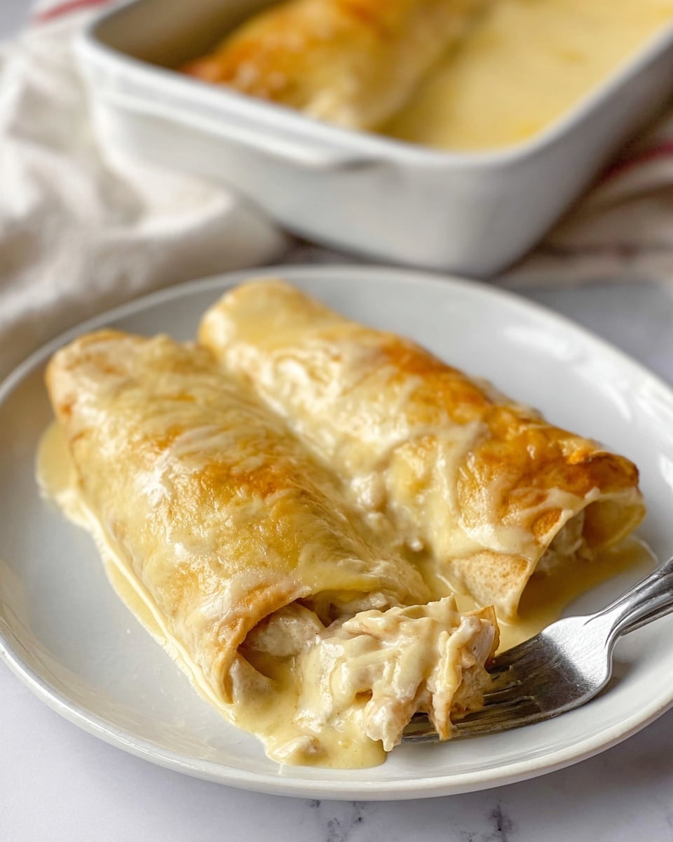 The image shows a white plate on a white marbled surface with two rolled enchiladas covered in a creamy, light yellow sauce that has a smooth and slightly shiny texture. One enchilada is slightly opened at the front, revealing a soft, creamy filling with small chunks inside. A silver fork is partially inserted into the opened enchilada, lifting a bite-sized piece. In the background, there is a white baking dish filled with more enchiladas covered in the same sauce. Photo taken with an iphone --ar 4:5 --v 7